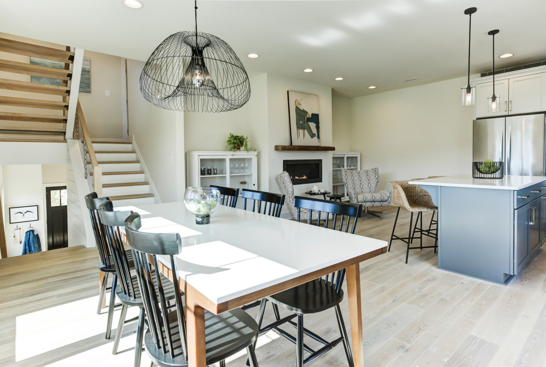 kitchen and dining room with light floors, fireplace, black lighting, open stairs and black chairs