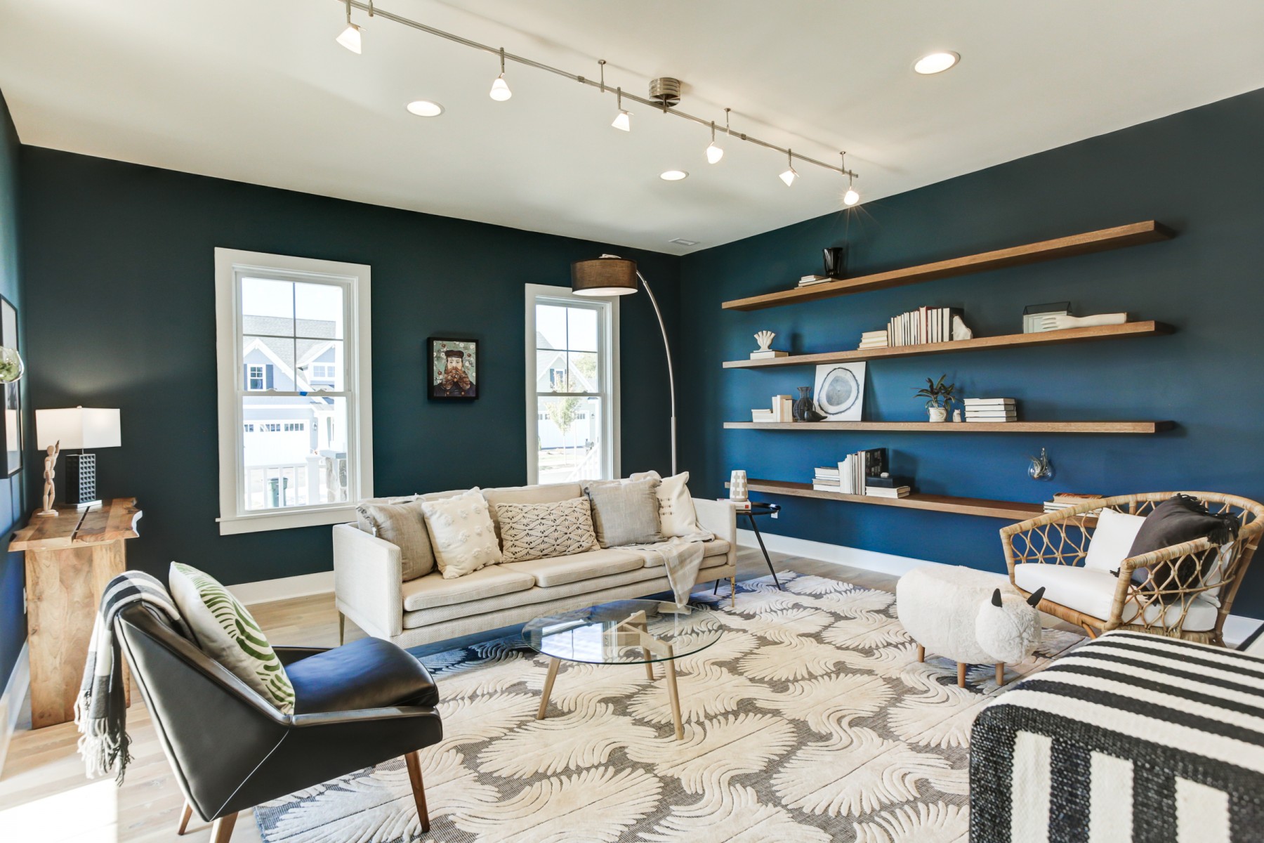 dark blue teal room with long built in shelves, sheep ottoman, black leather chair and rattan chair